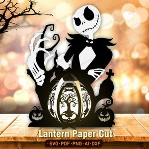 May include: A black and white paper cut design featuring a skeletal character with a round head and stitched mouth, wearing a suit. The scene includes a central lantern with tree silhouettes, two jack-o'-lanterns, and a tombstone with a cross.