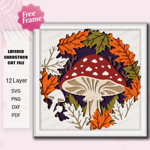 May include: A square layered cardstock cut file featuring a large red mushroom with white spots surrounded by orange, green, and white autumn leaves. The design includes text stating Free Frame, Layered Cardstock Cut File, 12 Layer, SVG, PNG, DXF, PDF.