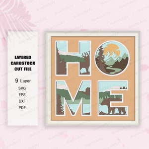 May include: Layered cardstock cut file design of the word "HOME" with a deer, bear, and mountain scene inside each letter. The design is in shades of brown, green, blue, and white.