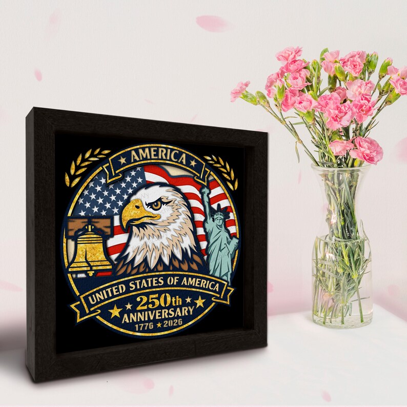 May include: A framed artwork commemorating the 250th anniversary of the United States of America. The design includes an eagle, the American flag, the Liberty Bell, and the Statue of Liberty. The frame is dark brown, and a vase of pink flowers is next to it.