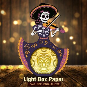 May include: A multi-layered paper light box design featuring a skeleton figure wearing a sombrero and playing a violin. The figure wears a dark purple dress with orange accents and a large circular cutout displaying a glowing yellow sugar skull.