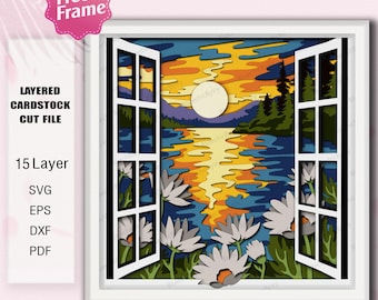 May include: A layered cardstock cut file depicting a sunset scene viewed through an open window. The artwork features a lake, mountains, trees, and flowers, with a bright sun. The image includes the text "Free Frame" and "Layered Cardstock Cut File".