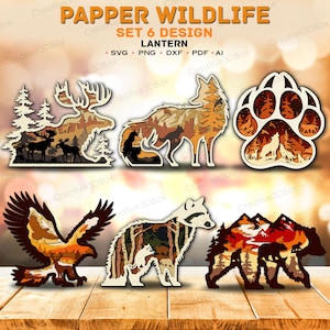 May include: A set of six layered paper lantern designs titled PAPPER WILDLIFE SET 6 DESIGN. The collection includes silhouettes of a moose, fox, paw print, eagle, raccoon, and bear, each filled with intricate forest and mountain landscape scenes.