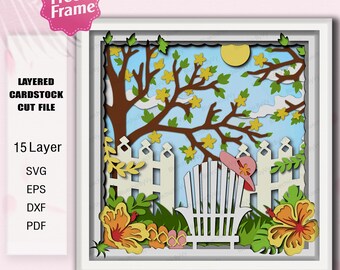 May include: A layered cardstock cut file featuring a sunny outdoor scene. The artwork includes a white picket fence, a tree with yellow flowers, a sun, and a beach chair with a pink hat. The image is framed in white and includes the text "Free Frame".