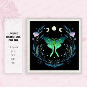 May include: A layered cardstock cut file design featuring a green luna moth with a dark green and blue floral wreath and three crescent moons on a black background.