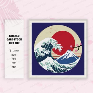 May include: A layered cardstock cut file design of a Japanese wave, Mount Fuji, and a red sun. The design is in a circle with a cream background and a blue border. The design is perfect for paper crafting and scrapbooking.