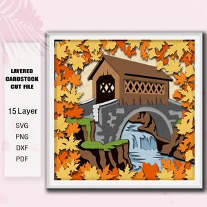 May include: A 15-layer cardstock cut file featuring a brown covered bridge over a blue waterfall, surrounded by orange and yellow autumn leaves. Text on the left reads: LAYERED CARDSTOCK CUT FILE, 15 Layer, SVG, PNG, DXF, PDF.