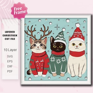 Op de afbeelding: Een gelaagd kartonnen snijbestand met drie katten in feestelijke kleding. Eén kat draagt een rendiergewei, een andere een groene muts en de derde een kerstmuts. Elke kat draagt een trui. De achtergrond is lichtblauw met sneeuwvlokken.