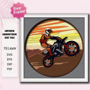 Op de afbeelding: Een gelaagde kartonnen snijbestand met een motorcrosser op een motorfiets tegen een zonsondergang. Het ontwerp heeft 15 lagen en is beschikbaar in SVG-, EPS-, DXF- en PDF-formaten. De afbeelding is omlijst.