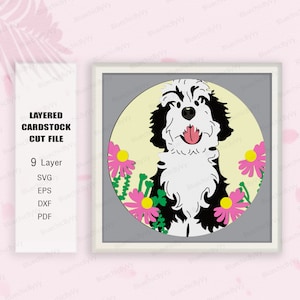 May include: A layered cardstock cut file featuring a smiling black and white dog with a pink tongue, surrounded by pink flowers and green stems, set against a light yellow circle and a gray background, framed in a white square.