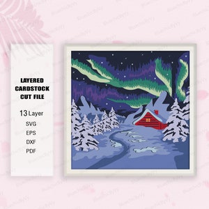 May include: A layered papercraft design featuring a red cabin in a snowy forest with a green and blue aurora borealis in the night sky. The design is made up of 13 layers and is available in SVG, EPS, DXF, and PDF formats.