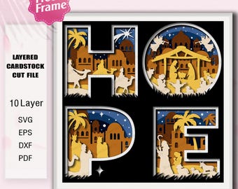 May include: A layered cardstock cut file design spelling "HOPE" with a nativity scene. The design features a 10-layer construction with illustrations of camels, angels, and a stable, all in shades of tan, brown, and blue. The image includes the text "Free Frame".