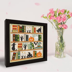 May include: A framed illustration of a bookshelf filled with books, pumpkins, candles, bats, a witch's hat, and a black cat. The bookshelf is decorated with a spooky Halloween theme.