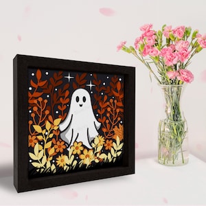 May include: A framed illustration of a white ghost in a field of orange, yellow, and brown leaves. The ghost has a smiling face and is surrounded by stars.