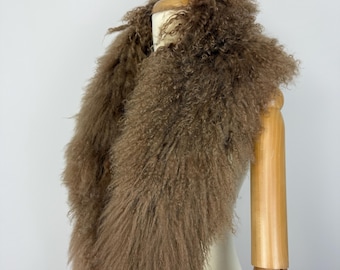 May include: A brown curly fur scarf draped over a wooden mannequin. The scarf features long, textured, and shaggy fibers that create a voluminous appearance around the neck and shoulders, showcasing a natural, earthy tone and dense pile.