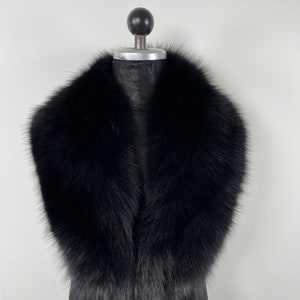 May include: A black faux fur collar with a wide, rounded shape. The collar is made of soft, fluffy fur and is designed to be worn around the neck.