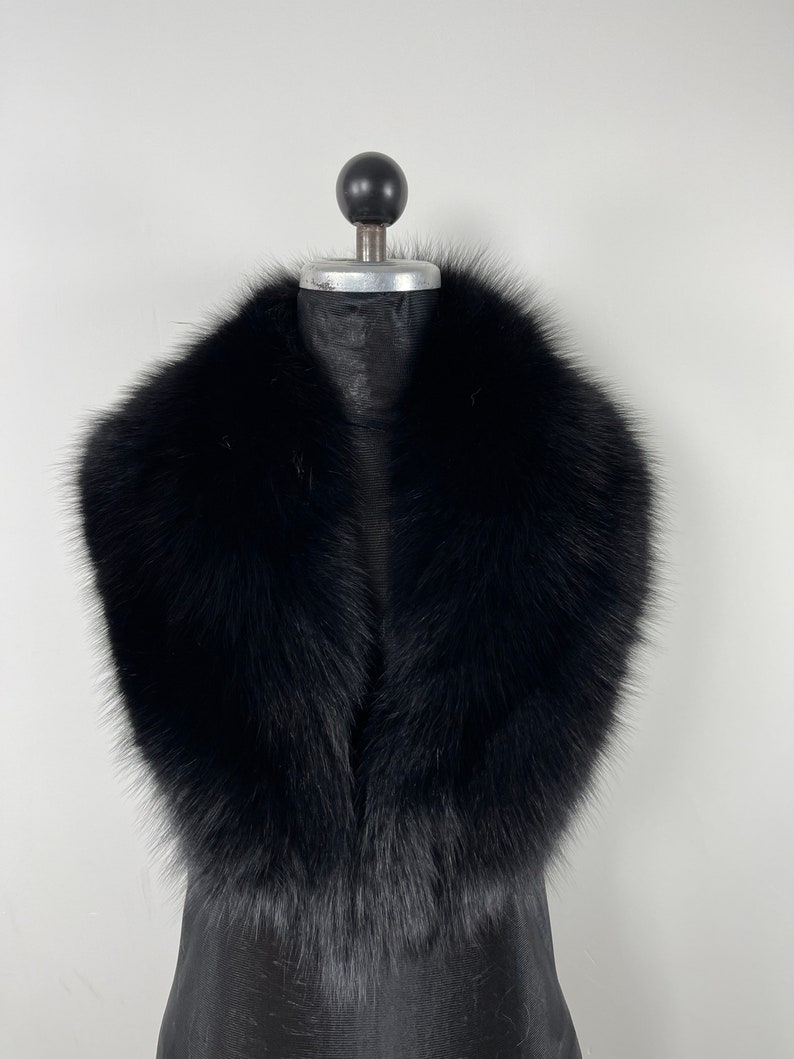 May include: A black faux fur collar with a wide, rounded shape. The collar is made of soft, fluffy fur and is designed to be worn around the neck.