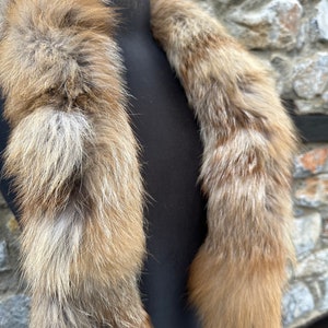 May include: A long, fluffy fox fur scarf in shades of brown and white. The scarf is displayed on a black mannequin.