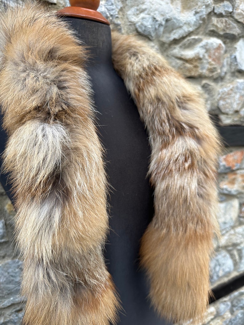 May include: A long, fluffy fox fur scarf in shades of brown and white. The scarf is displayed on a black mannequin.