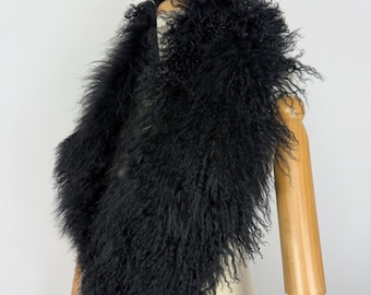 May include: A black scarf made of long, curly, textured fur draped over a wooden mannequin. The scarf features a dense, shaggy appearance with fine, wispy strands that create a voluminous silhouette around the neck and shoulders of the form.
