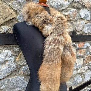 May include: A long, brown and white fur scarf with two tails. The scarf is draped around a black mannequin's neck.