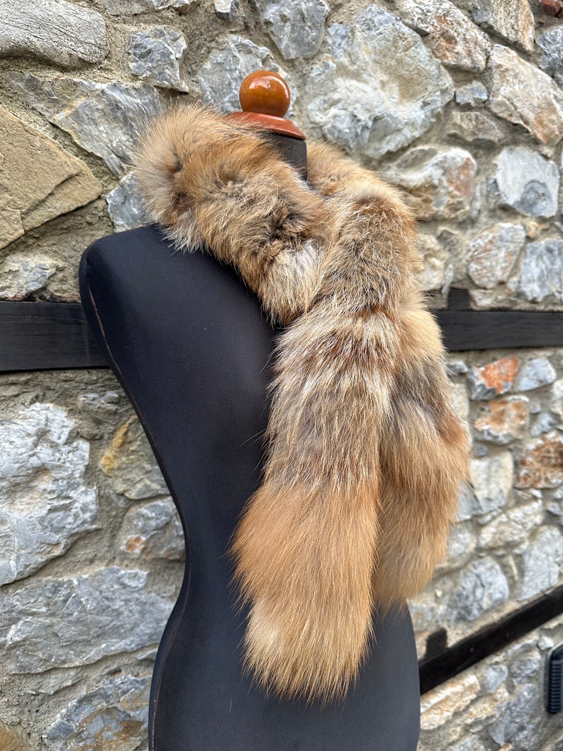 May include: A long, brown and white fur scarf with two tails. The scarf is draped around a black mannequin's neck.