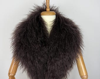May include: A dark brown, long-haired, shaggy fur collar draped around the neck of a mannequin. The collar features a dense, textured appearance with fine, wispy strands of hair extending outward, creating a voluminous and layered look.