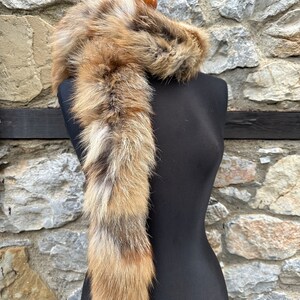 May include: A long, brown and white fur scarf with a fluffy texture. The scarf is draped over a black mannequin.