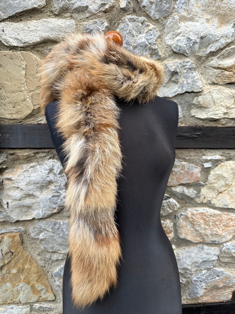 May include: A long, brown and white fur scarf with a fluffy texture. The scarf is draped over a black mannequin.