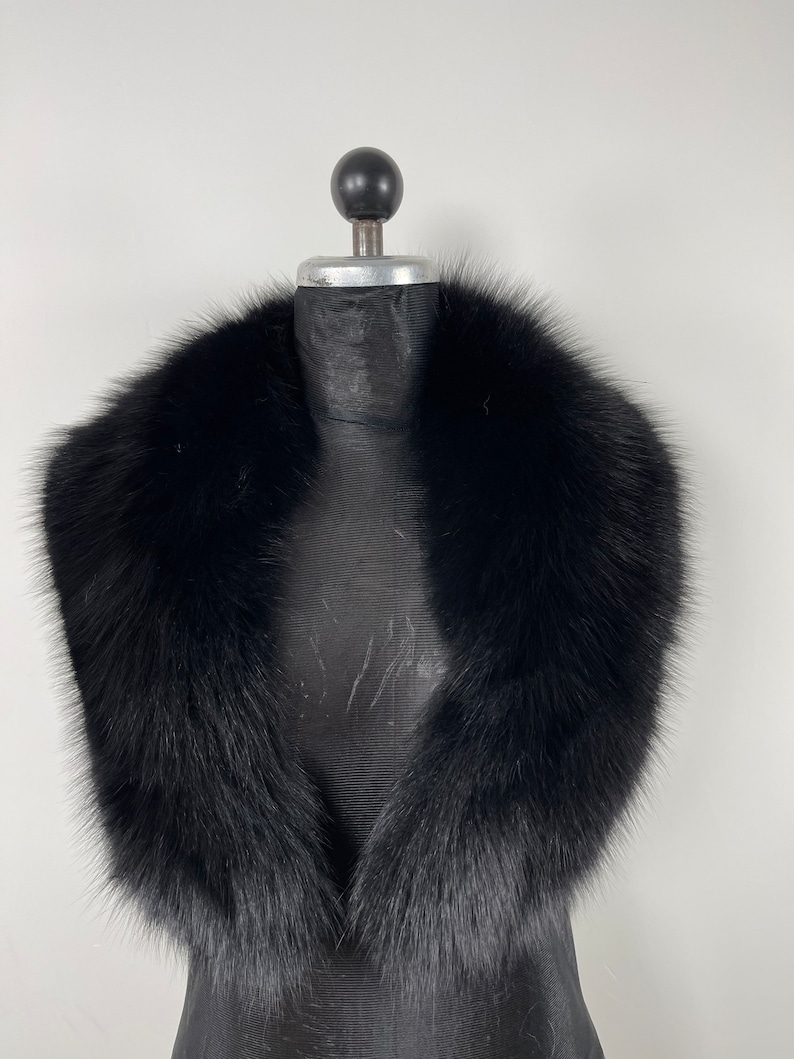 May include: A black faux fur collar for a coat or jacket. The collar is made of soft, fluffy fur and has a classic design.
