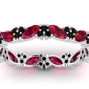 May include: A silver ring with alternating red and black gemstones. The ring is set with marquise-cut red stones and small black stones, forming a continuous pattern around the band.