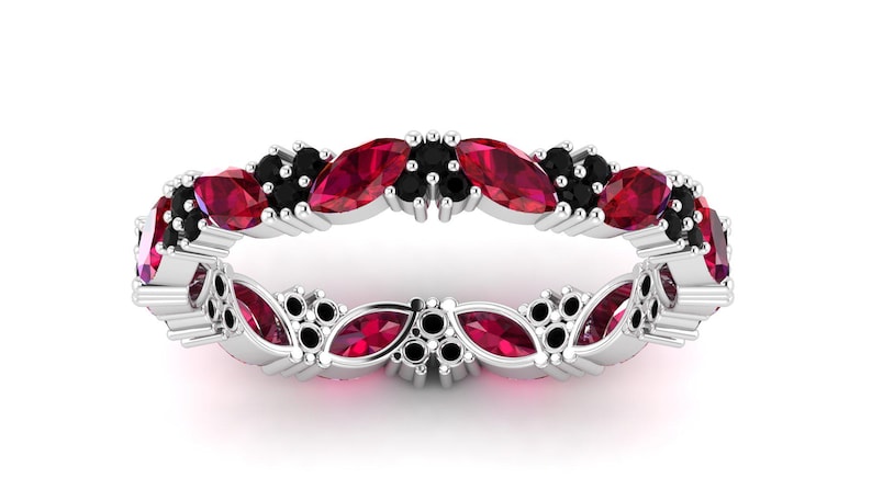 May include: A silver ring with alternating red and black gemstones. The ring is set with marquise-cut red stones and small black stones, forming a continuous pattern around the band.
