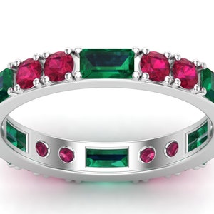 May include: A silver band ring with alternating emerald green and ruby red gemstones. The ring is set with emerald green rectangular stones and ruby red round stones.