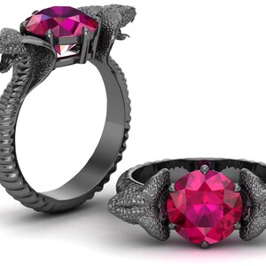 Könnte beinhalten: Zwei Ringe, einer aufrecht und einer auf der Seite, mit einem Schlangendesign. Die Ringe sind dunkelgrau mit einer strukturierten Oberfläche. Jeder Ring hat einen großen, oval geschliffenen, leuchtend rosa Edelstein. Die Schlangenköpfe bilden die Fassung für die Edelsteine.