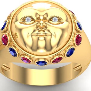 Puede incluir: Anillo dorado con un diseño detallado de rostro con dos pequeños diamantes como ojos. El anillo está adornado con piedras preciosas rojas y azules alternas. El anillo tiene un acabado liso y pulido. Joyería.