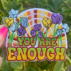 May include: A colorful embroidered patch with a rainbow arch and flowers. The patch says "You Are Enough" in a retro font.