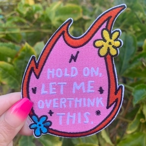 May include: Pink embroidered iron-on patch shaped like a flame with the text "Hold on, let me overthink this." and two embroidered flowers.