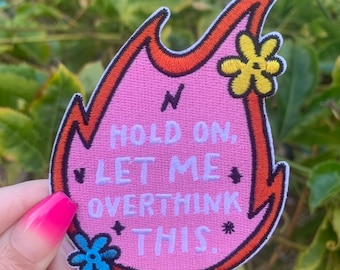 May include: Pink embroidered iron-on patch shaped like a flame with the text "Hold on, let me overthink this." and two embroidered flowers.