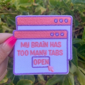 May include: A white embroidered patch with a purple border, depicting a web browser window with the text "My brain has too many tabs open".