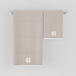 May include: Two beige towels with white embroidered geometric designs hanging on a silver towel rack.