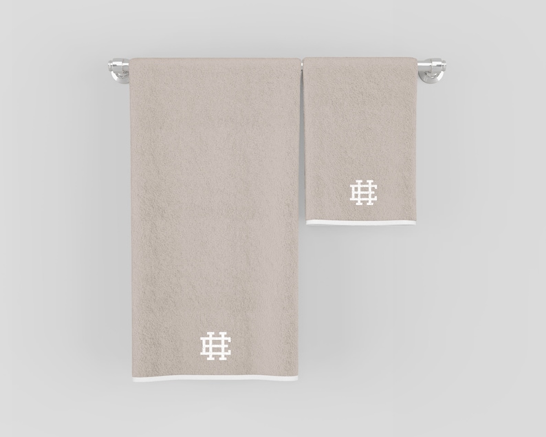 May include: Two beige towels with white embroidered geometric designs hanging on a silver towel rack.