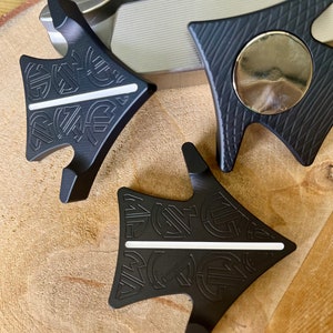 Puede incluir: Dos herramientas de alineación de putter de golf negras con una línea blanca en el centro. Las herramientas tienen forma de flecha y tienen una superficie texturizada.