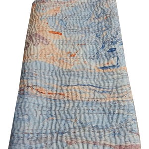 Op de afbeelding: Een blauwe en oranje kantha-deken met een marmerpatroon. De deken is gemaakt van katoen en heeft een zachte, gestikte textuur.