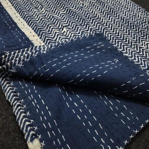 May include: A blue and white kantha quilt with a chevron pattern. The quilt is hand-stitched and has a frayed edge.