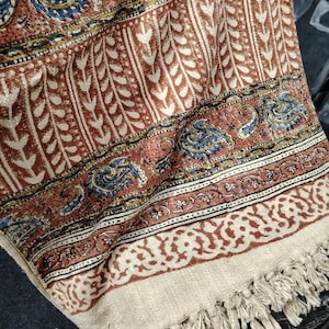 Könnte beinhalten: Eine braune und cremefarbene Wolldecke mit Paisley- und Blumenmuster. Die Decke hat einen Fransenrand.
