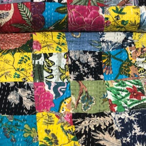 May include: A patchwork quilt featuring a variety of rectangular fabric panels with diverse floral and botanical prints in vibrant colours including yellow, red, blue, green, and black, all joined by visible white running stitch embroidery.