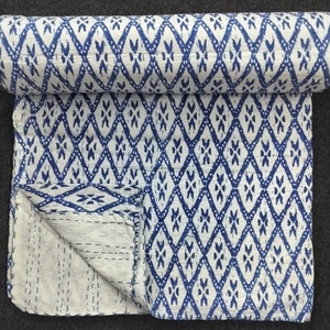 Peut inclure: Une courtepointe kantha blanche et bleue avec un motif en losange. La courtepointe est pliée en deux et repose sur une surface grise.