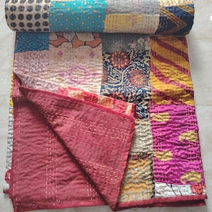 May include: A patchwork quilt featuring a variety of colorful fabric squares with diverse patterns including floral, paisley, and geometric designs. The quilt is partially rolled at the top and displays a solid deep red fabric on the underside.