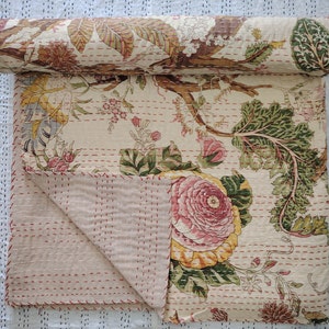 Peut inclure: Une courtepointe kantha en coton blanc avec un motif floral dans des tons de rose, vert et marron. La courtepointe est pliée en deux et présente un détail de couture rouge.
