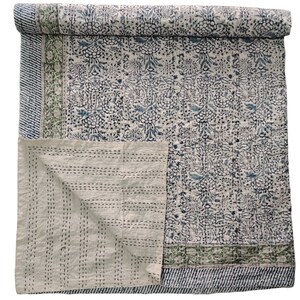 May include: A white cotton quilt with a blue floral pattern and green border. The quilt is folded in half and the inside is visible.